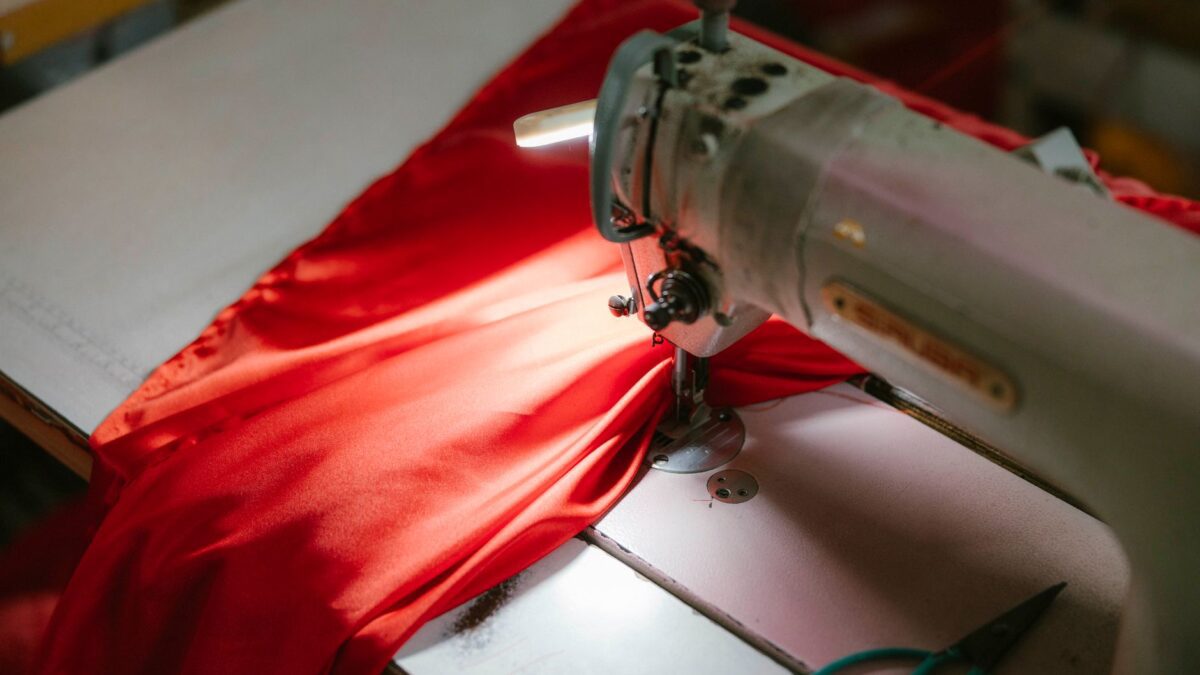Werktisch mit Nähmaschine, Stoffen und Notizblock in einer kleinen Werkstatt