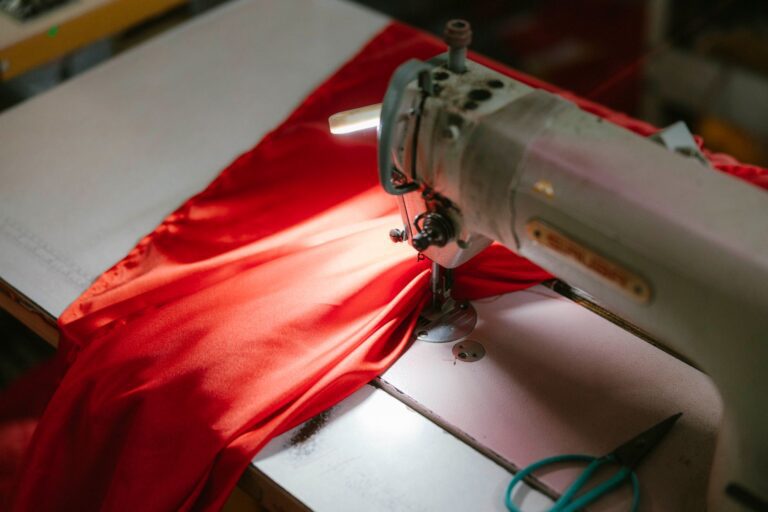 Werktisch mit Nähmaschine, Stoffen und Notizblock in einer kleinen Werkstatt